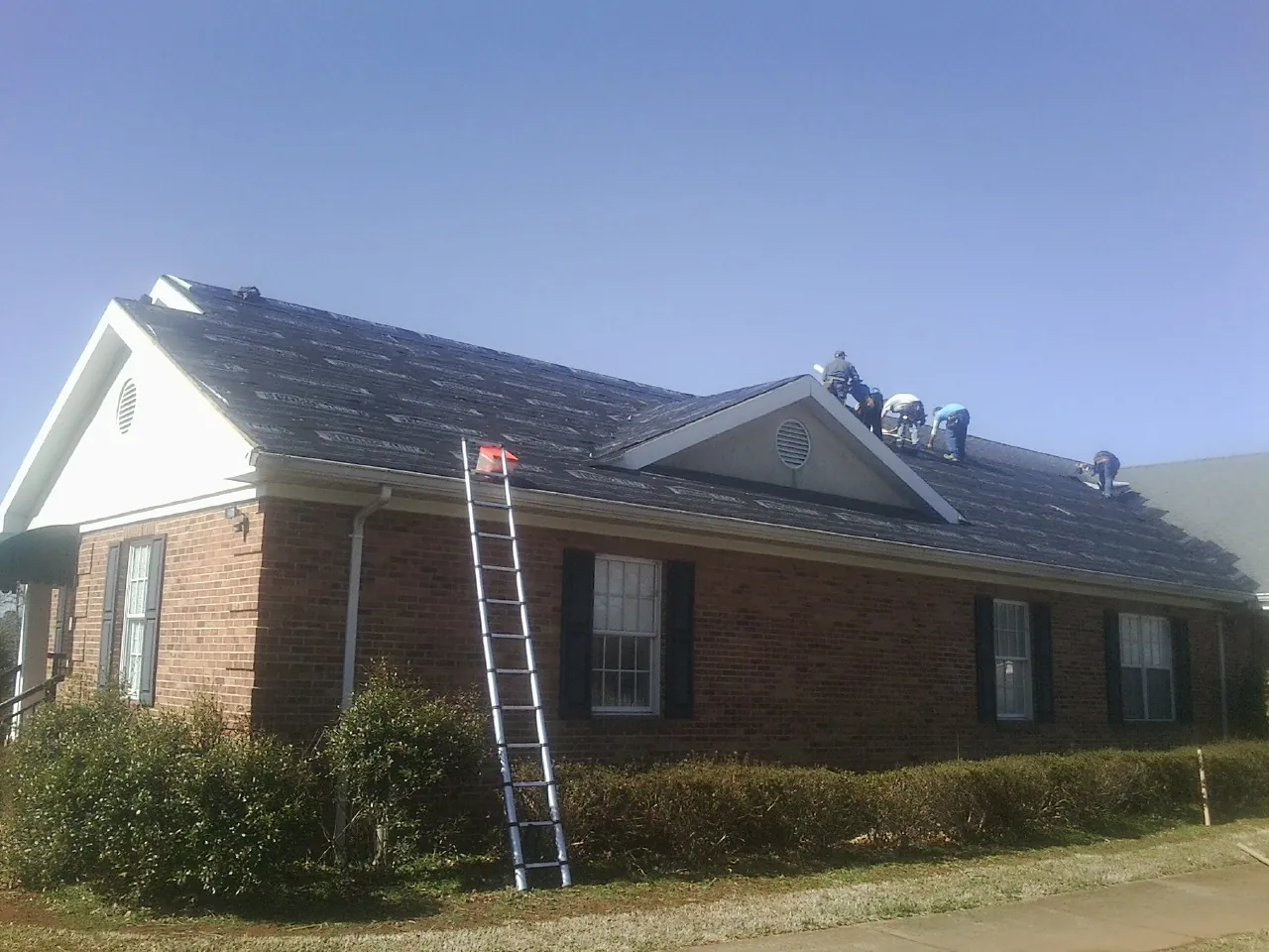 Crew tearing shingles off a brick ranch roof with a ladder set — Metal Roof Repair work by our crew in Stormville