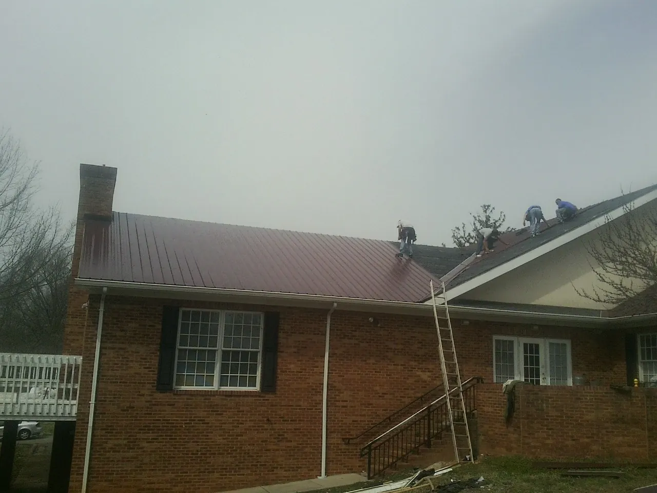 Crew setting red metal roofing panels on a brick home in Stormville