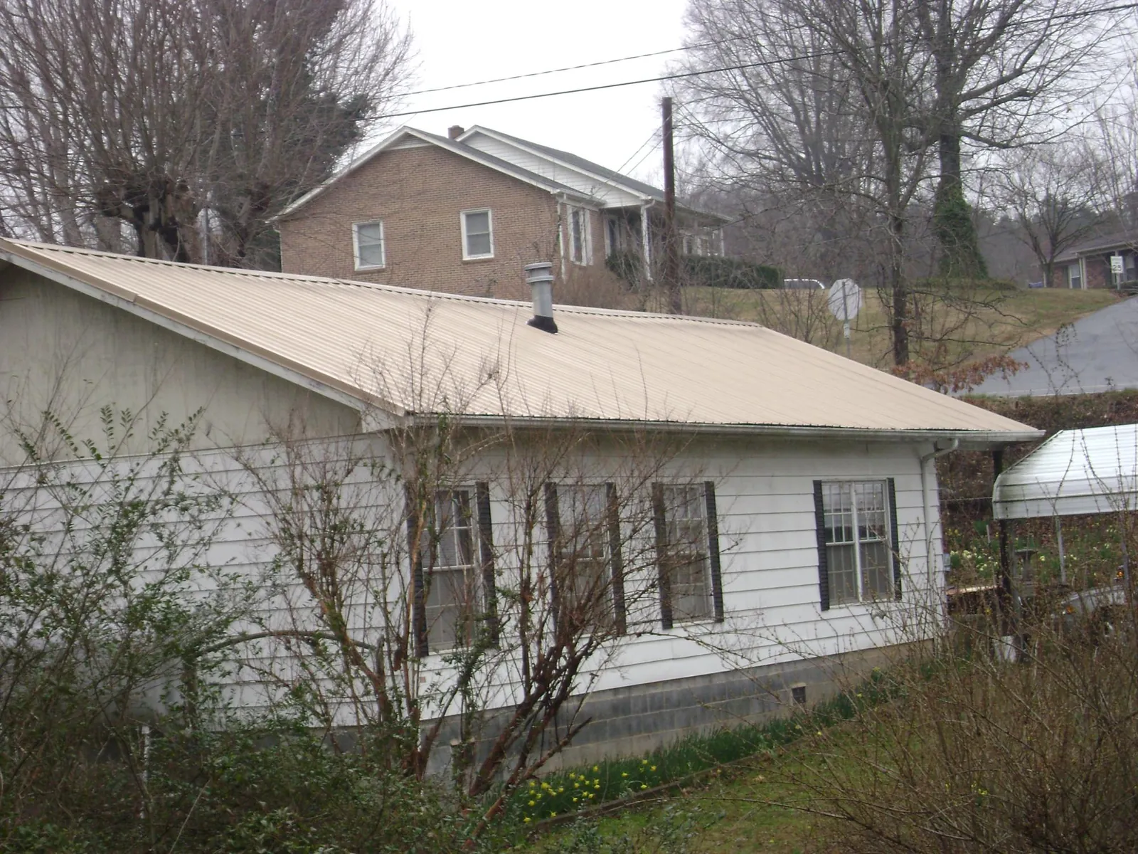 Tan metal roof on a white sided house set into a hillside — Commercial Roofing by Roofing Brothers in Stormville